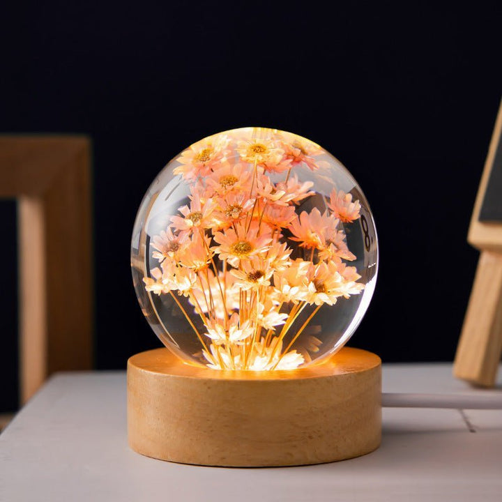 Klare Kristallkugel Lampe mit kunstvoll arrangierten Ewigen Blumen, sanftem LED-Licht auf Holzsockel.