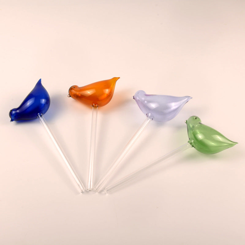 Hand platziert einen Glasvogel-Wasserspender in die Erde, für einfache Urlaubsbewässerung Ihrer Blumen.