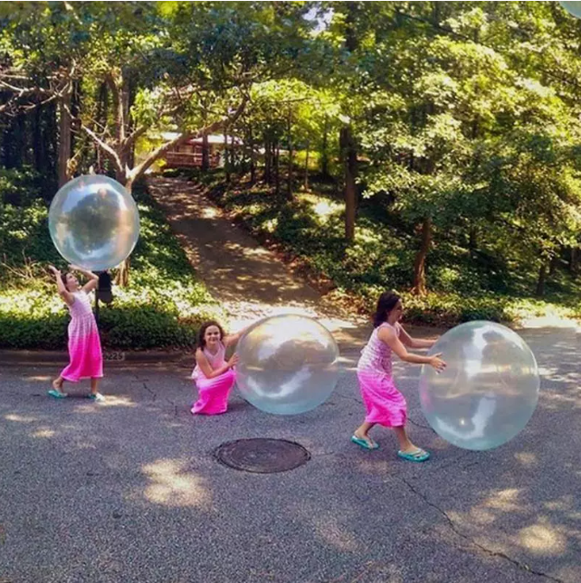 Freunde spielen zusammen mit dem großen, bunten Bubble-Ball im Park; aktives Outdoor-Spielzeug für Gruppenspaß.
