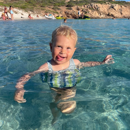 Fröhliches Kind mit SicherPlatsch Schwimmlernhilfe, ideal für erste Schwimmversuche & Wassersicherheit.