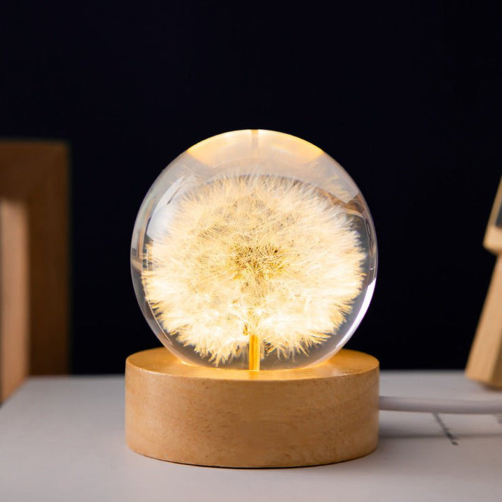 Kristallkugel-Lampe mit leuchtender 3D-Löwenzahnblume und elegantem Holzsockel als Stimmungslicht.
