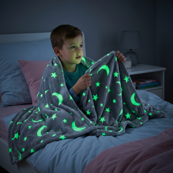 Detailansicht der leuchtenden Kuscheldecke: Sterne und Mondmuster auf grau-rosa Stoff, glow in the dark Effekt.