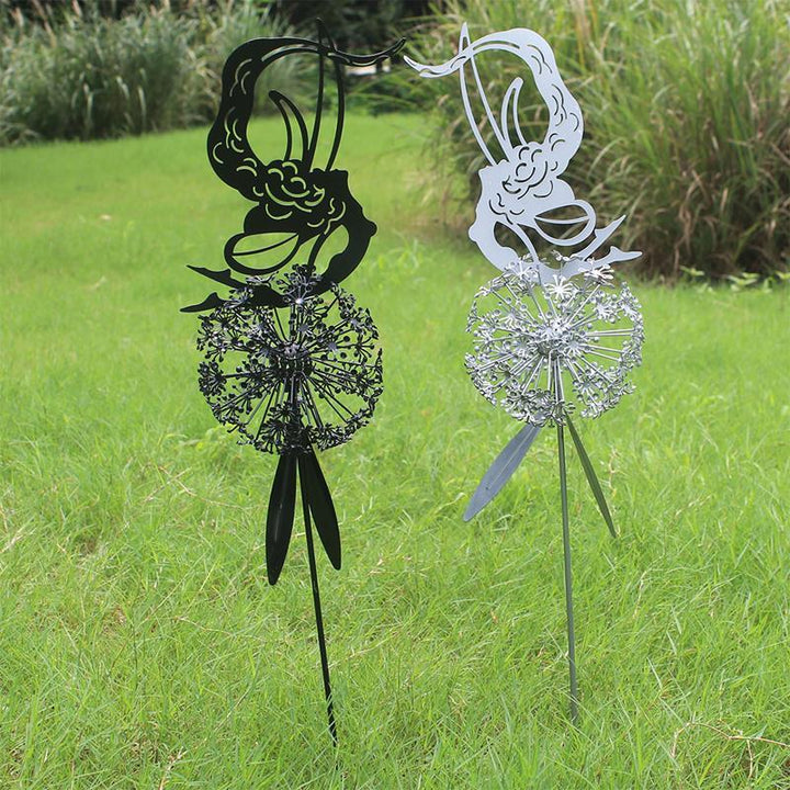 Nahaufnahme: filigrane Fee schwebt über Löwenzahn, charmante Garten-Skulptur aus Metallkunst.