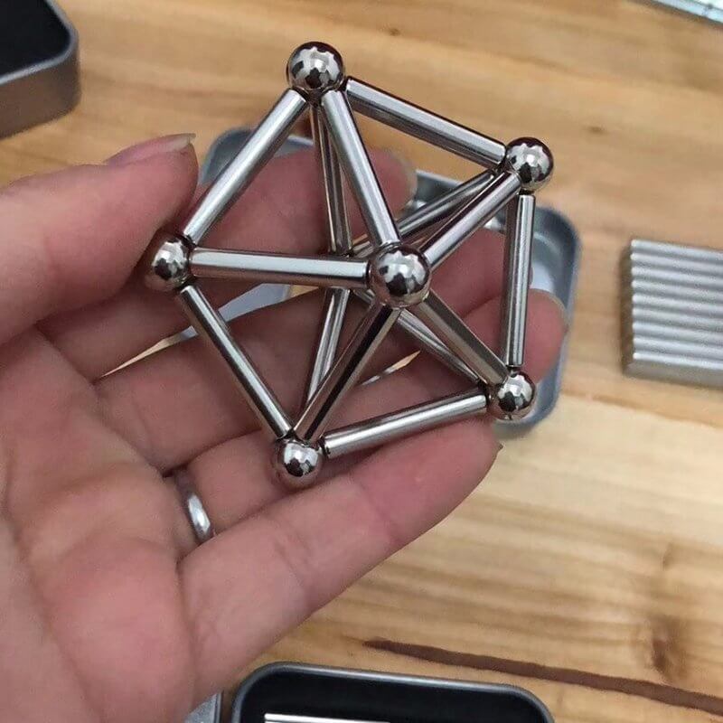 Kind baut mit Magneten: Eine Hand verbindet bunte Magnetstäbe & Metallkugeln zu einer stabilen Konstruktion.
