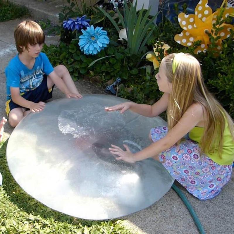 Kind lacht und spielt mit dem riesigen, dehnbaren Bubble Ball im Grünen. Outdoor-Spielspaß garantiert.