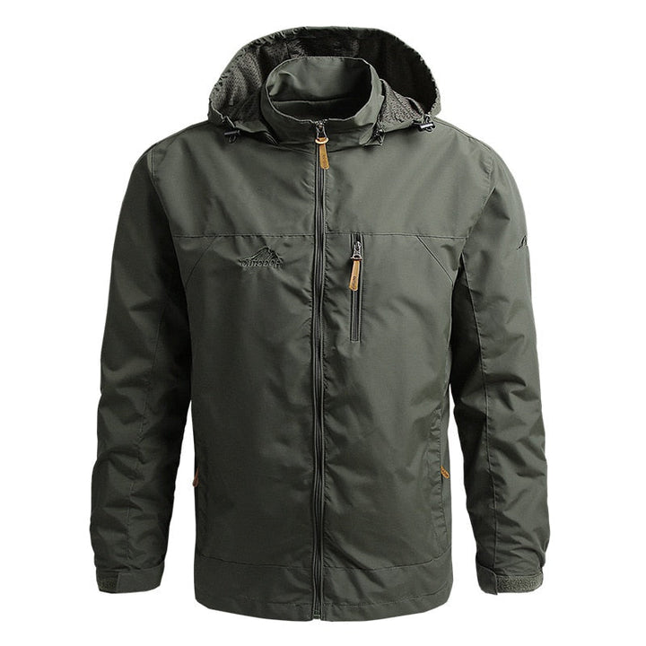Mann in taktischer, wasserdichter Herren Outdoorjacke mit Kapuze beim Wandern in den Bergen.