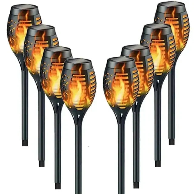 Solar-Gartenfackeln mit Flammeneffekt beleuchten einen dunklen Garten bei Nacht, als sichere Wegeleuchten.