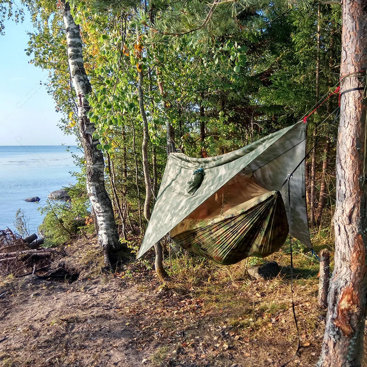 Camping Hängematte im Wald, gespannt zwischen Bäumen, mit schützendem Moskitonetz.