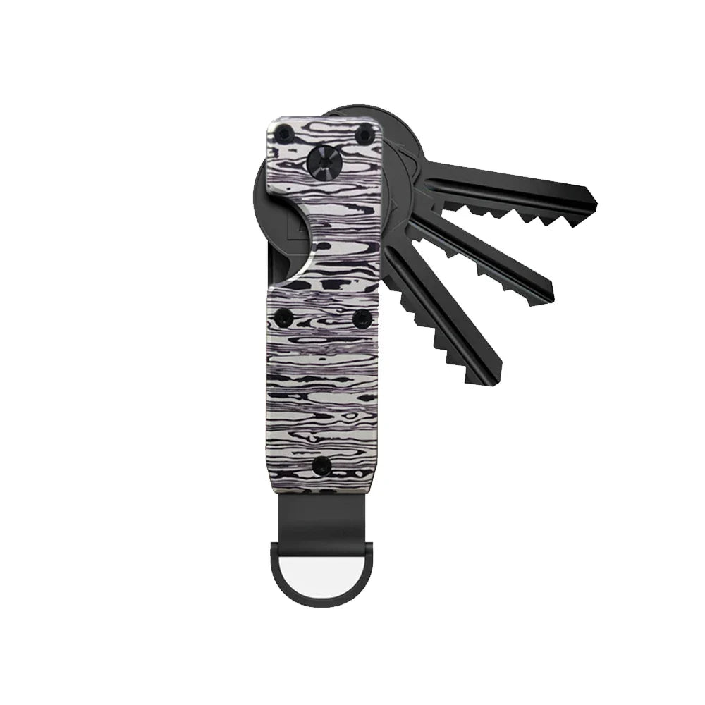 Aluminium Schlüssel Organizer als Teil des Taschenzubehörs, neben Portemonnaie und Handy platziert.