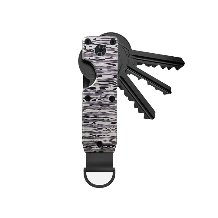 Aluminium Schlüssel Organizer als Teil des Taschenzubehörs, neben Portemonnaie und Handy platziert.