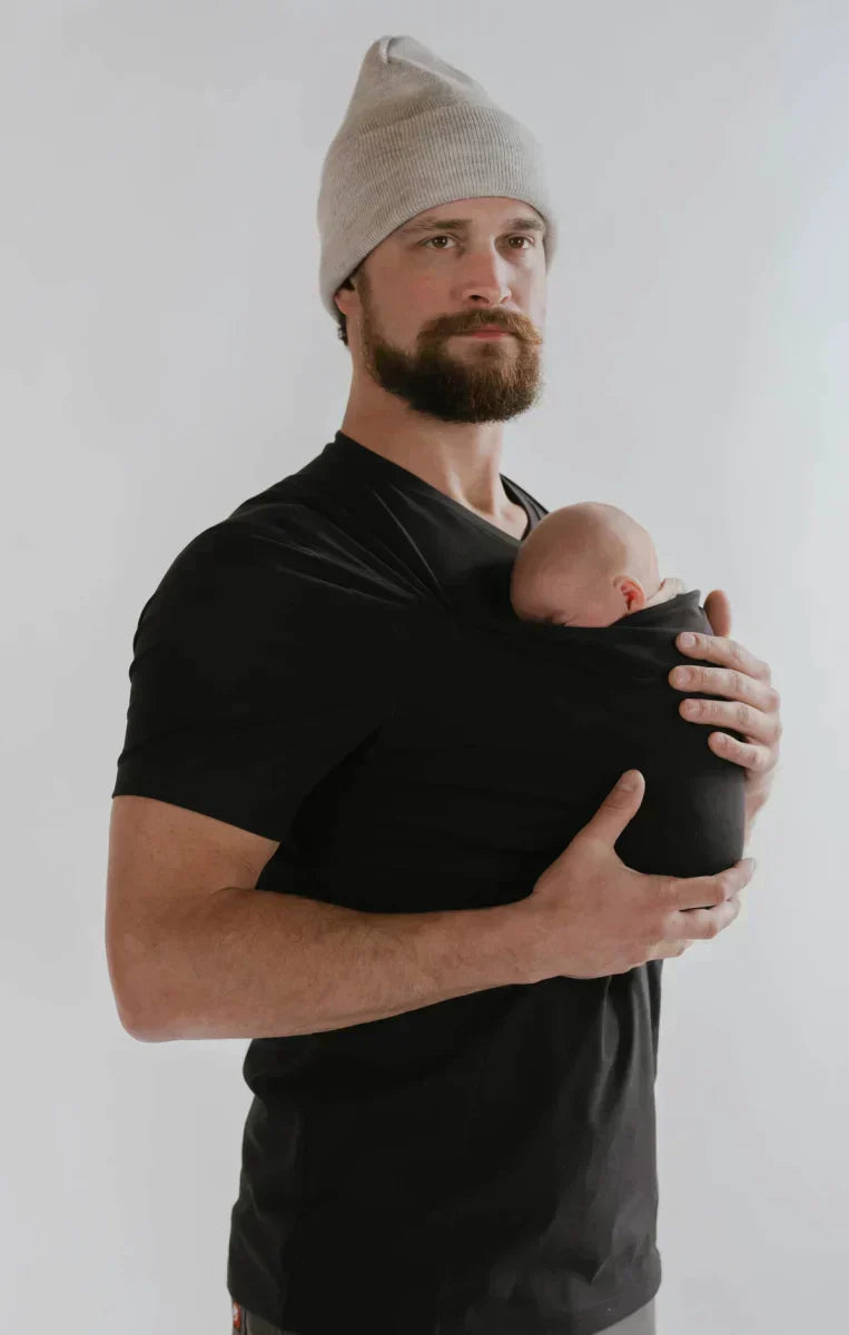 Glückliche Mutter trägt Baby mühelos im schwarzen Tragetuch T-Shirt; Hände frei, maximaler Komfort.